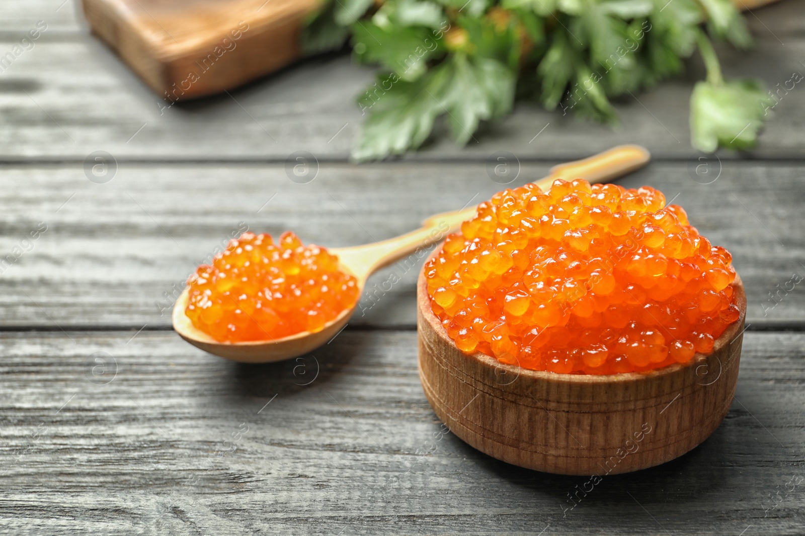 Photo of Bowl and spoon with delicious red caviar on wooden background