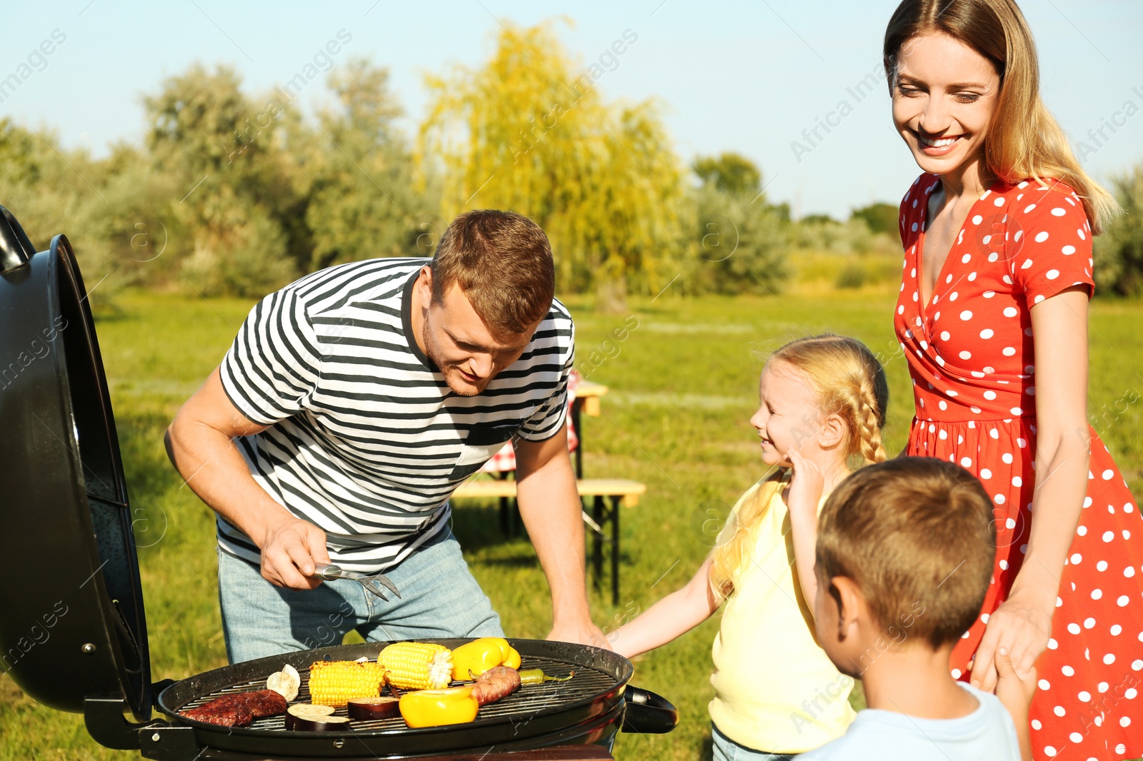 Photo of Happy family with little children having barbecue in park