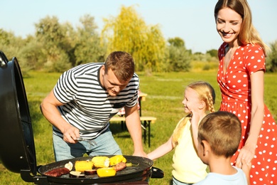 Photo of Happy family with little children having barbecue in park