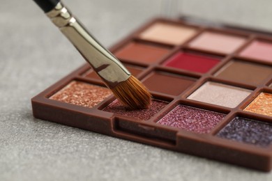 Photo of Colorful eyeshadow palette with brush on grey table, closeup view
