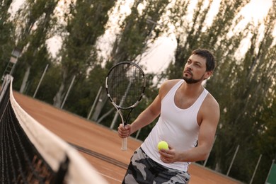 Handsome man with tennis racket and ball on court outdoors