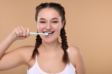 Woman with braces cleaning teeth on beige background. Space for text
