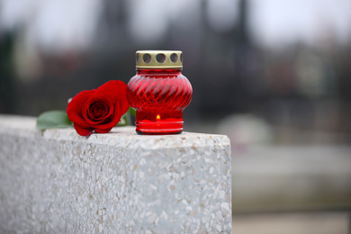 Photo of Red rose and candle on light grey granite tombstone outdoors. Funeral ceremony