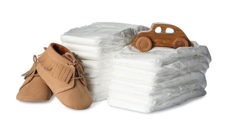 Photo of Disposable diapers, toy car and child's shoes on white background