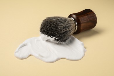 Photo of Brush with shaving foam on beige background, closeup