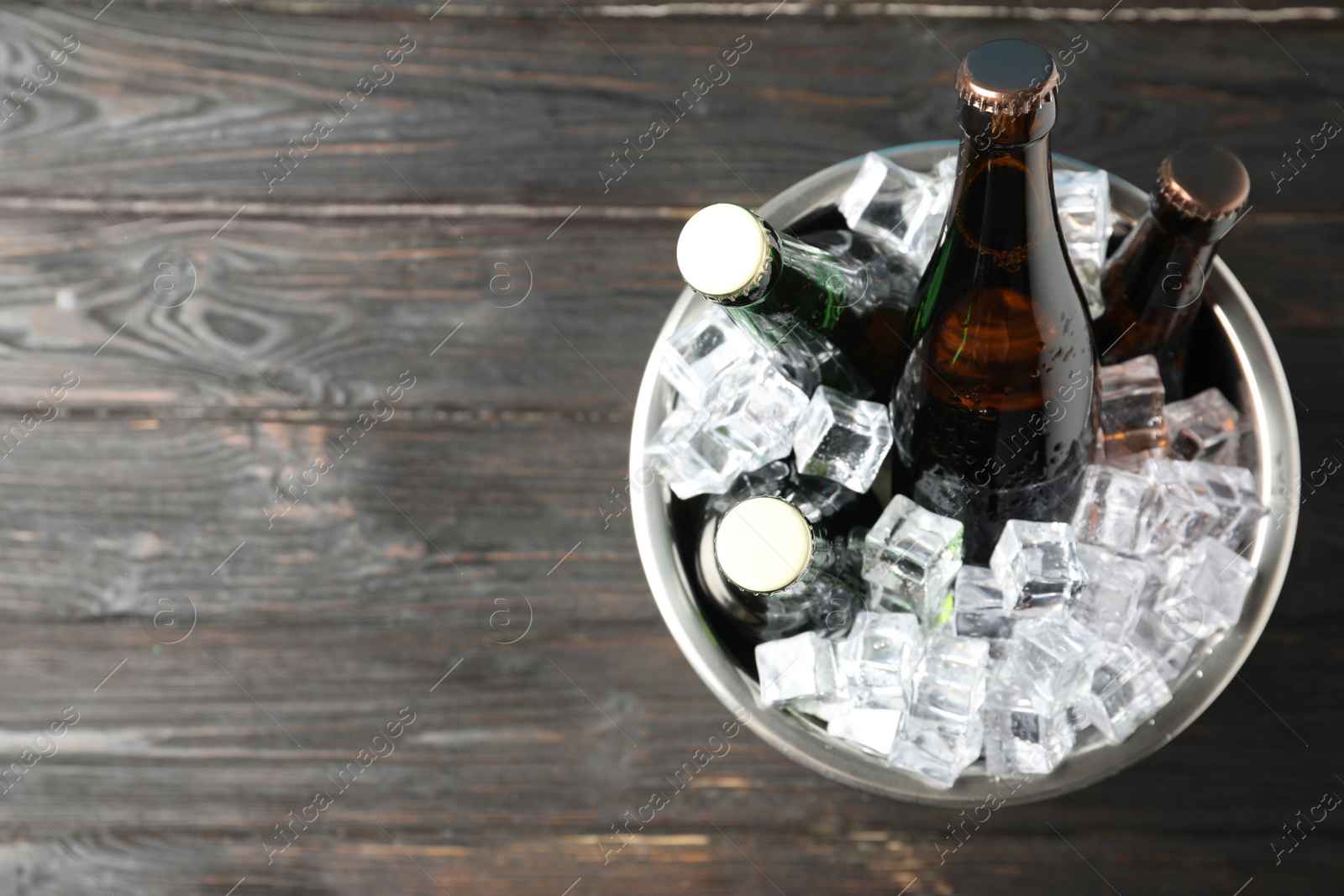 Photo of Metal bucket with bottles of beer and ice cubes on black wooden background, top view. Space for text