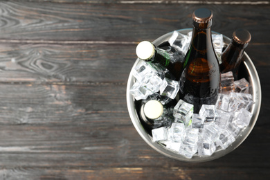 Photo of Metal bucket with bottles of beer and ice cubes on black wooden background, top view. Space for text