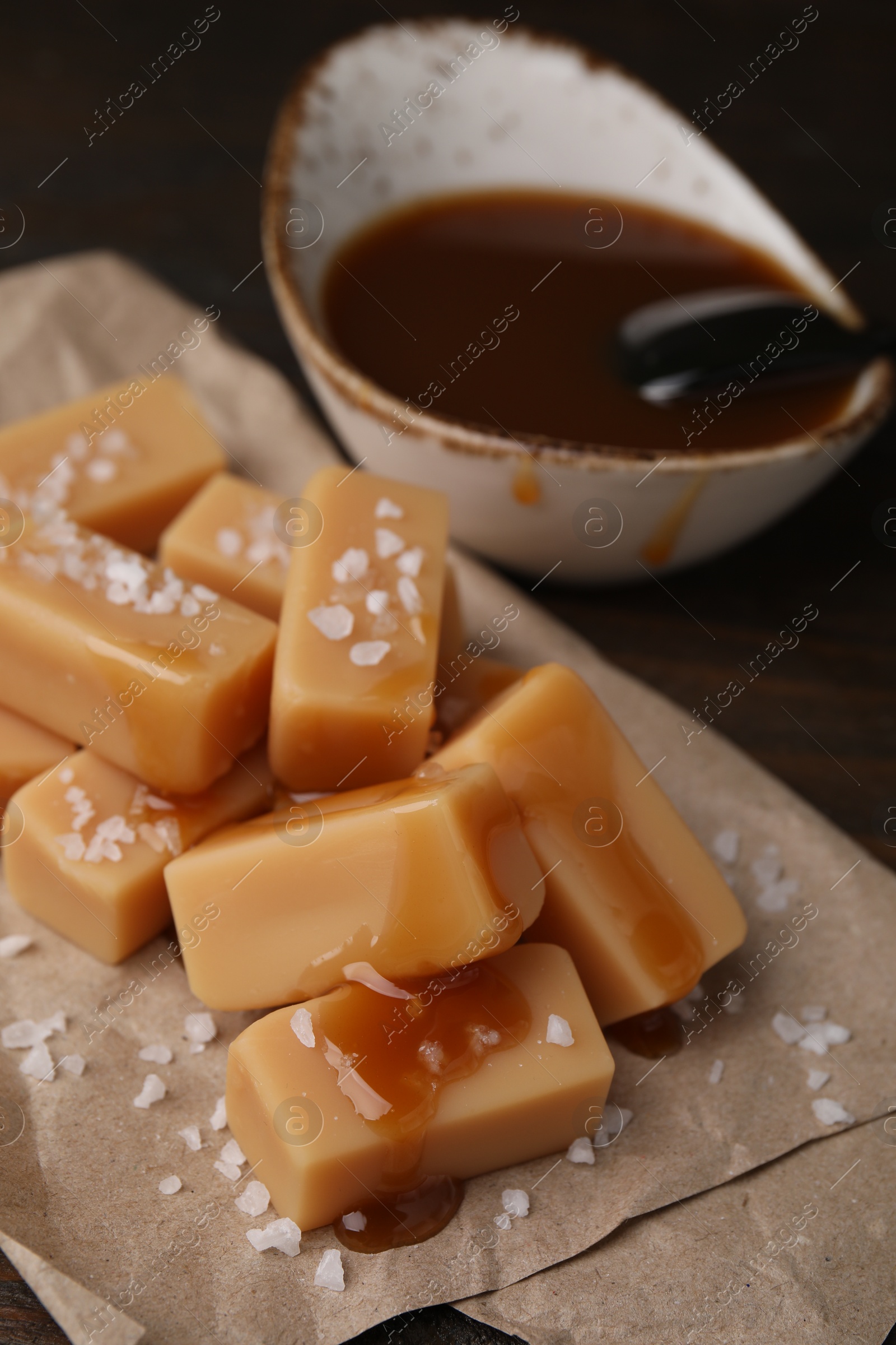 Photo of Delicious candies with sea salt and caramel sauce on wooden table, closeup