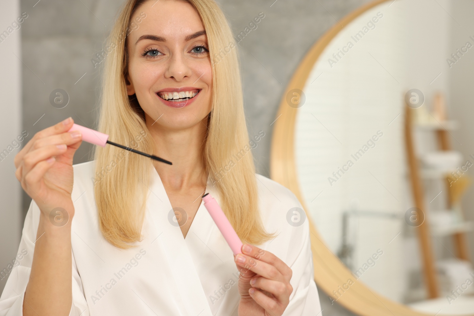 Photo of Beautiful happy woman with mascara in bathroom, space for text