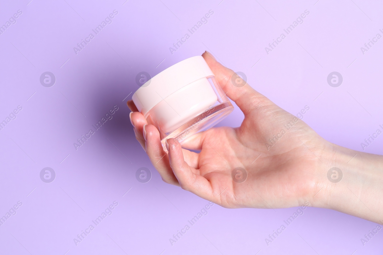 Photo of Woman holding jar of cream on violet background, closeup