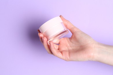 Woman holding jar of cream on violet background, closeup