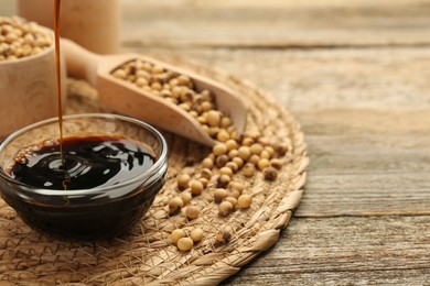 Pouring soy sauce into bowl at wooden table, closeup. Space for text