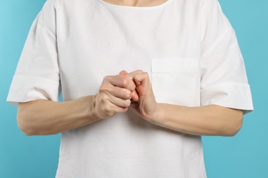 Woman cracking her knuckles on turquoise background, closeup. Bad habit