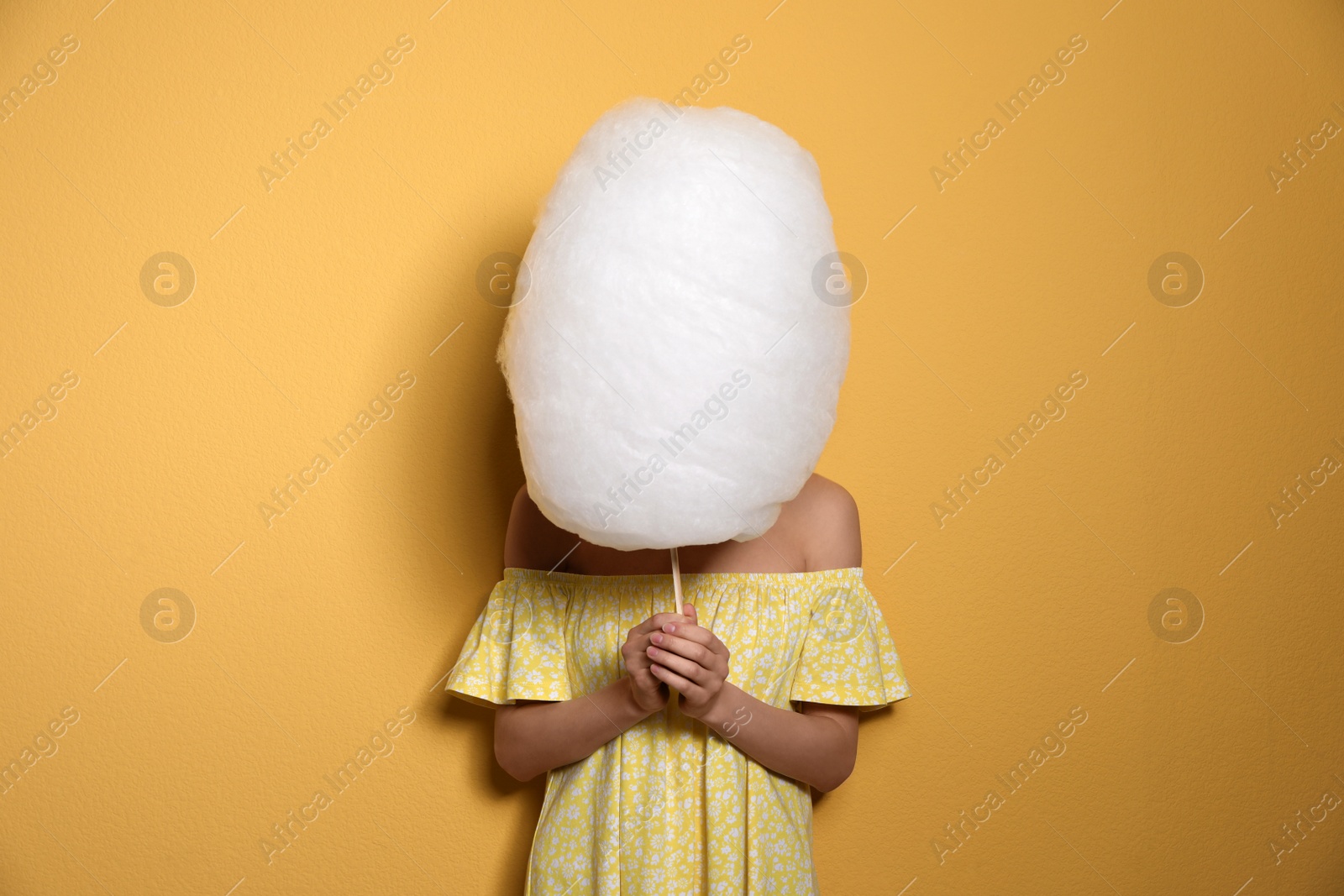 Photo of Young woman hiding behind tasty cotton candy on yellow background