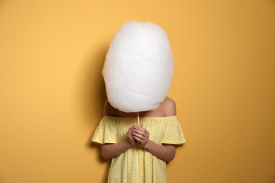 Photo of Young woman hiding behind tasty cotton candy on yellow background