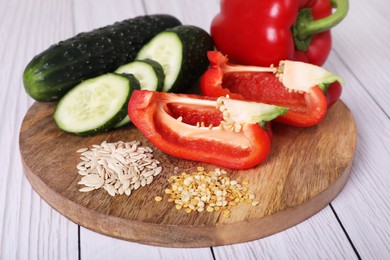 Photo of Fresh cucumbers, red bell peppers and vegetable seeds on white wooden table, closeup