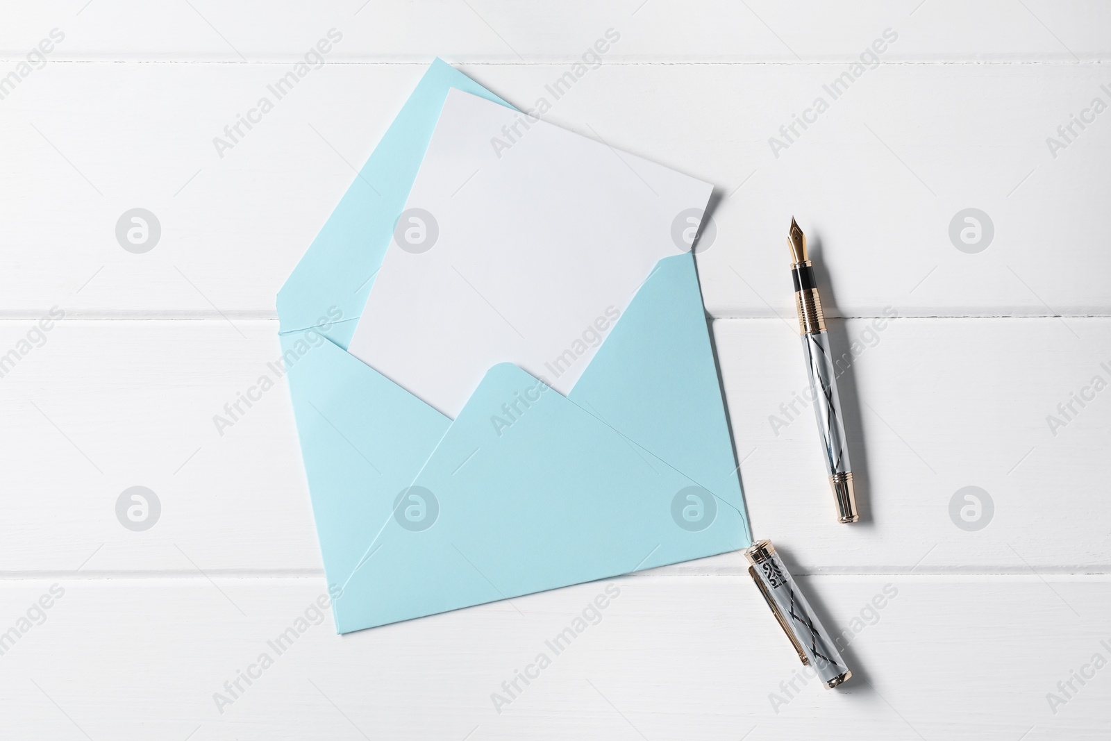 Photo of Blank sheet of paper, pen and letter envelope on white wooden table, top view