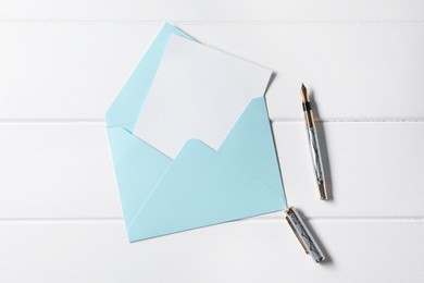 Photo of Blank sheet of paper, pen and letter envelope on white wooden table, top view