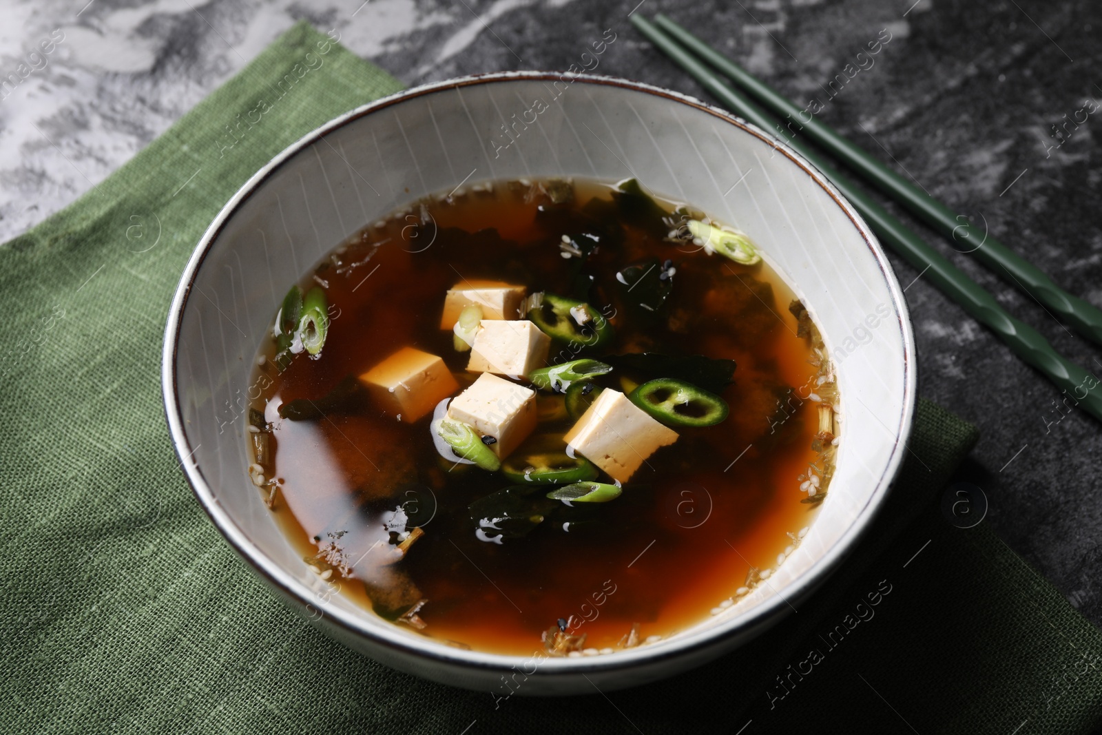 Photo of Bowl of delicious miso soup with tofu and chopsticks on black textured table