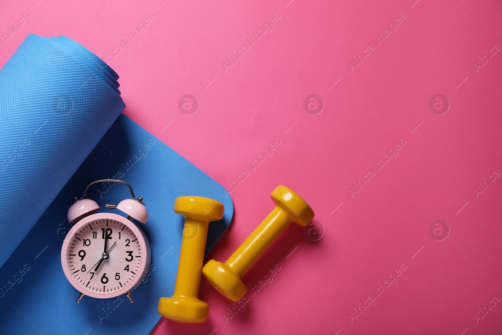 Photo of Fitness mat, dumbbells and alarm clock on pink background, flat lay with space for text. Morning exercise