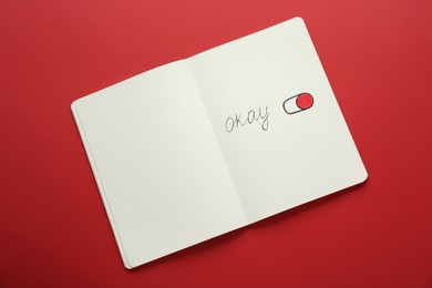 Photo of Notebook with word Okay and drawing of switch on button against red background, top view