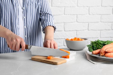Photo of Woman cutting fresh ripe juicy carrots at light grey table, closeup