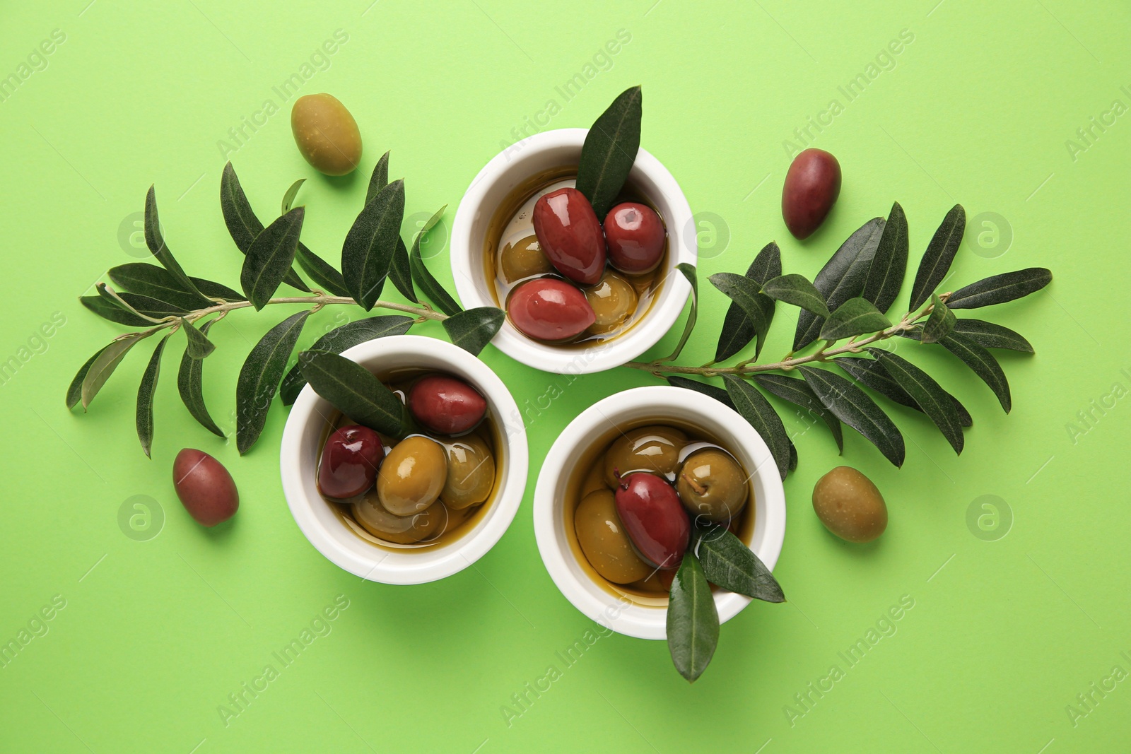 Photo of Bowls with different ripe olives and leaves on light green background, flat lay