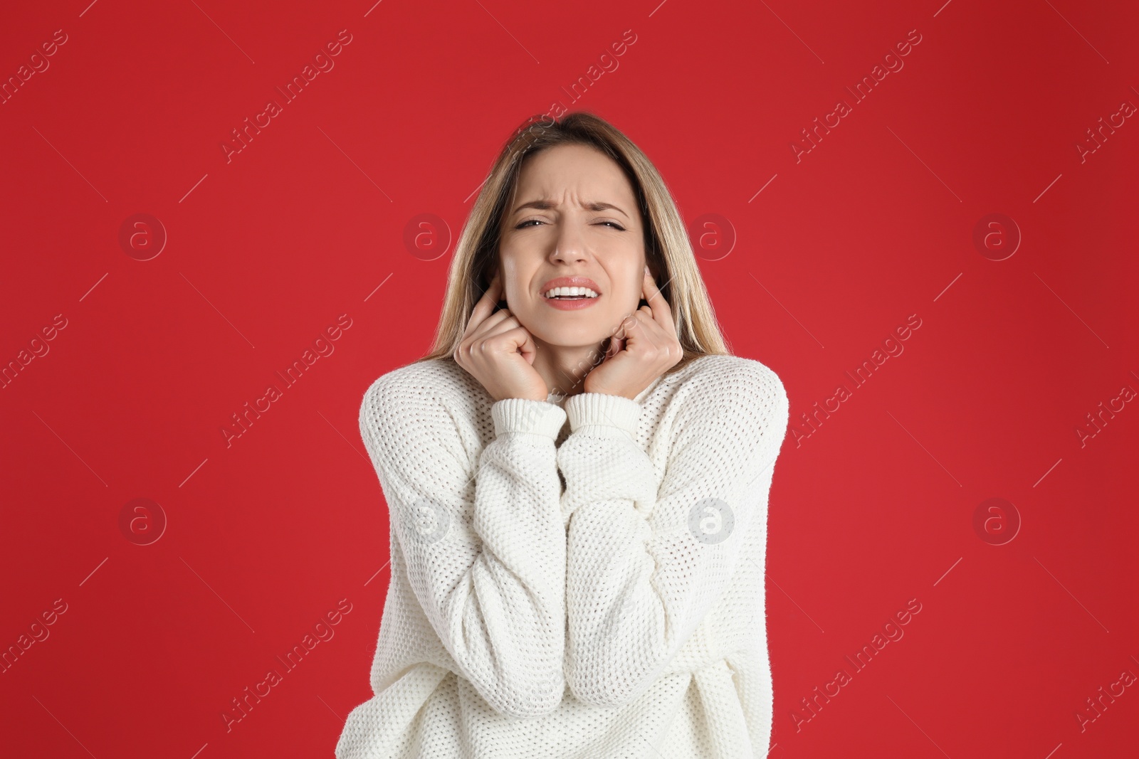 Photo of Emotional young woman covering her ears with fingers on red background