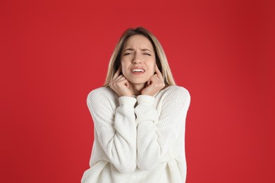 Photo of Emotional young woman covering her ears with fingers on red background