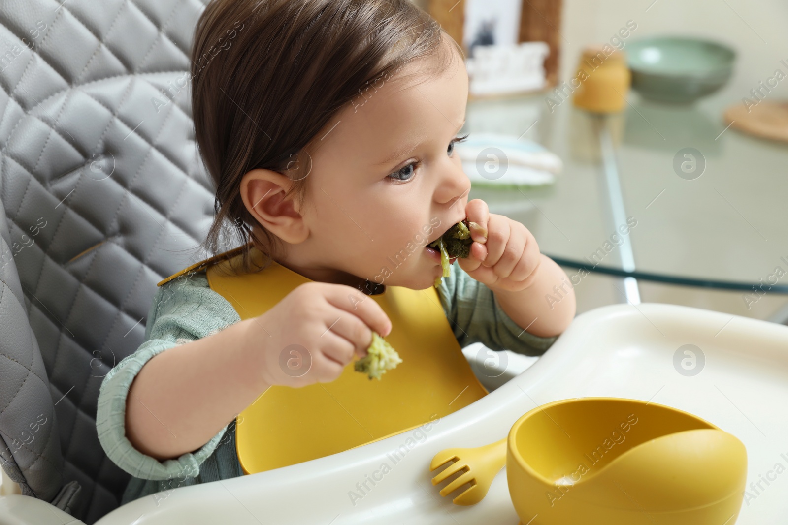Photo of Cute little baby eating healthy food in high chair indoors