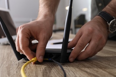 Photo of Man connecting cable to router at wooden table indoors, closeup. Wireless internet communication