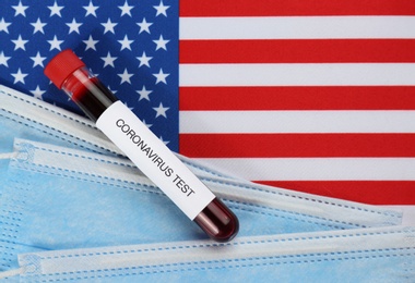 Test tube with blood and protective masks on American flag, flat lay. Coronavirus pandemic in USA