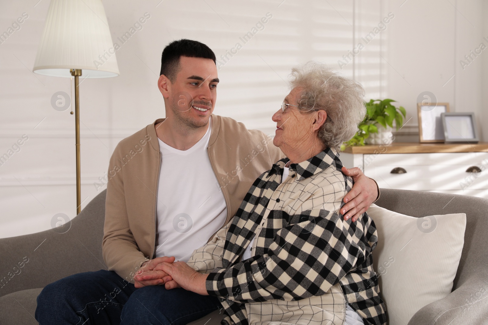 Photo of Young caregiver talking to senior woman in living room. Home health care service