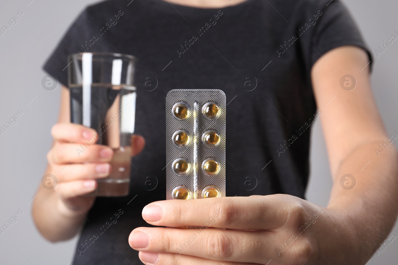 Photo of Woman holding pills in blister pack and glass of water on gray background, closeup