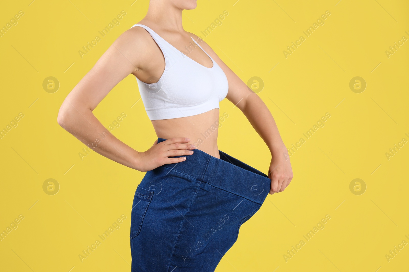 Photo of Young slim woman wearing oversized jeans on yellow background, closeup