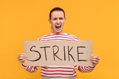 Photo of Screaming woman holding cardboard banner with word Strike on orange background
