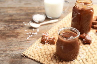 Photo of Jar of caramel sauce on wooden table. Space for text