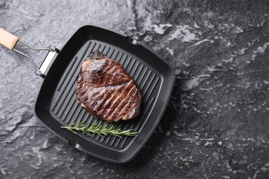 Grill pan with delicious fried beef meat and rosemary on grey textured table, top view. Space for text