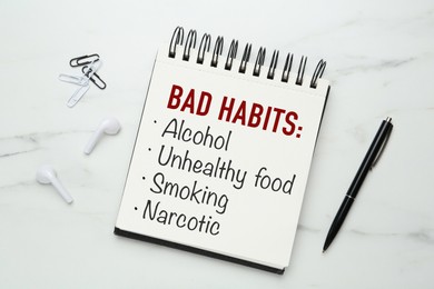 Image of Notebook with list of bad habits and pen on white marble table, flat lay. Change your lifestyle