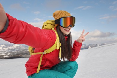 Image of Smiling woman in ski goggles taking selfie in snowy mountains