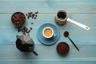 Coffee maker, jezve, beans, powder and cup of drink on light blue wooden table, flat lay