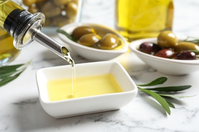 Pouring fresh olive oil into bowl on table