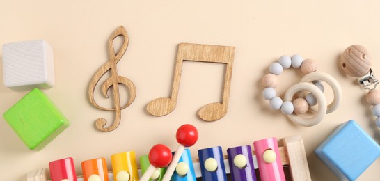 Baby song concept. Wooden notes, kids xylophone and toys on beige background, flat lay