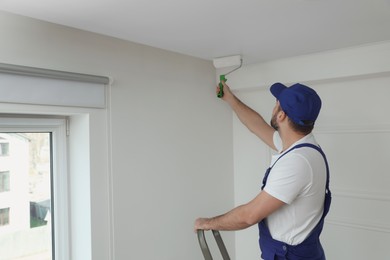 Photo of Handyman painting ceiling with white dye indoors, space for text