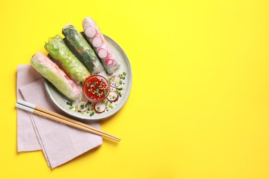 Photo of Delicious spring rolls served with sauce on yellow background, flat lay. Space for text