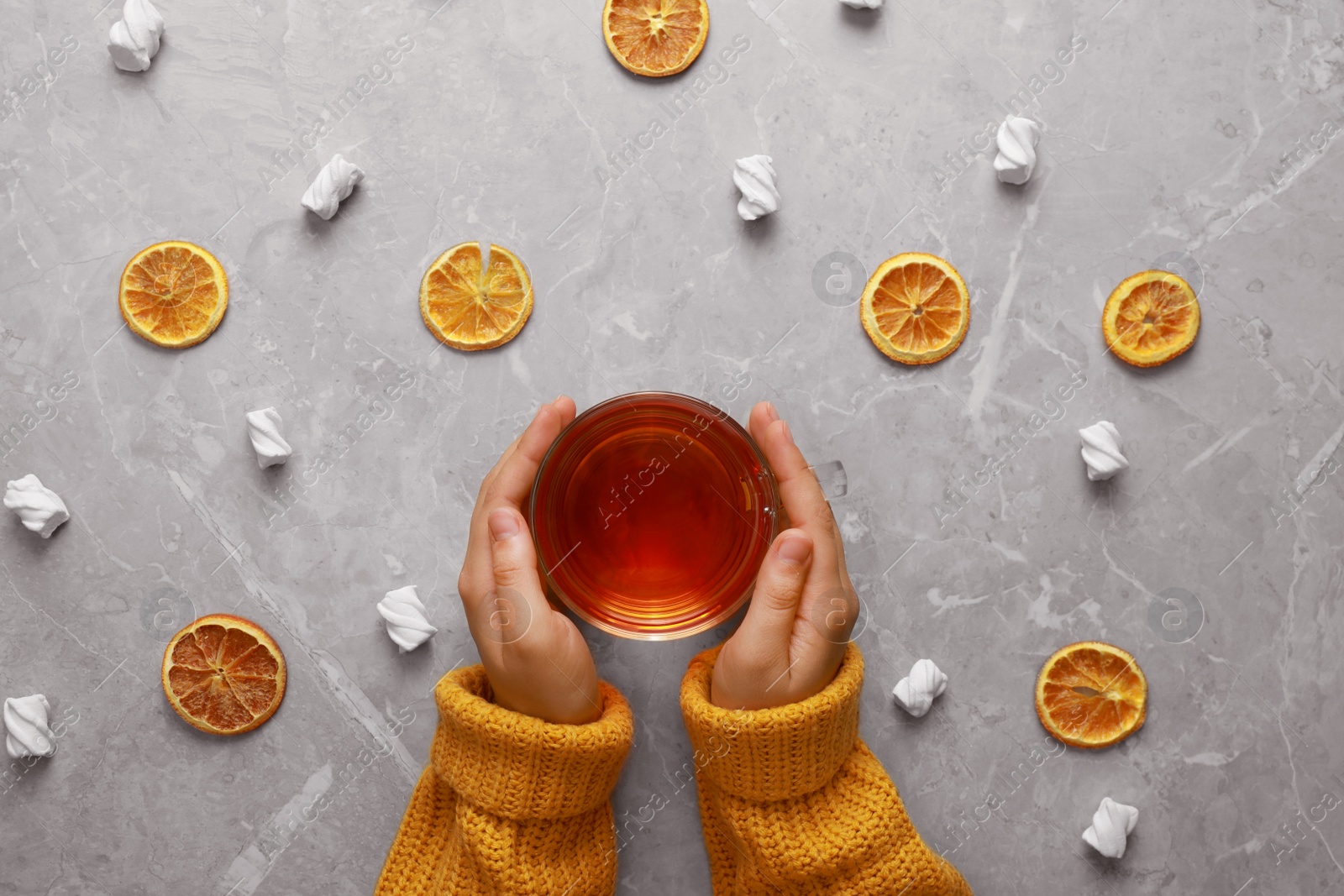 Photo of Woman holding cup of hot tea at grey marble table, top view. Cozy winter