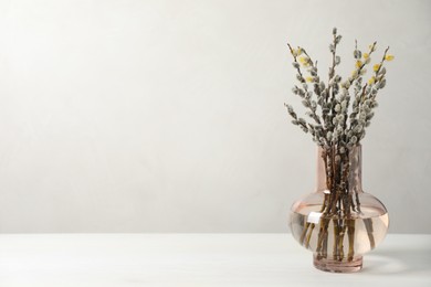 Photo of Beautiful pussy willow branches in vase on white table, space for text