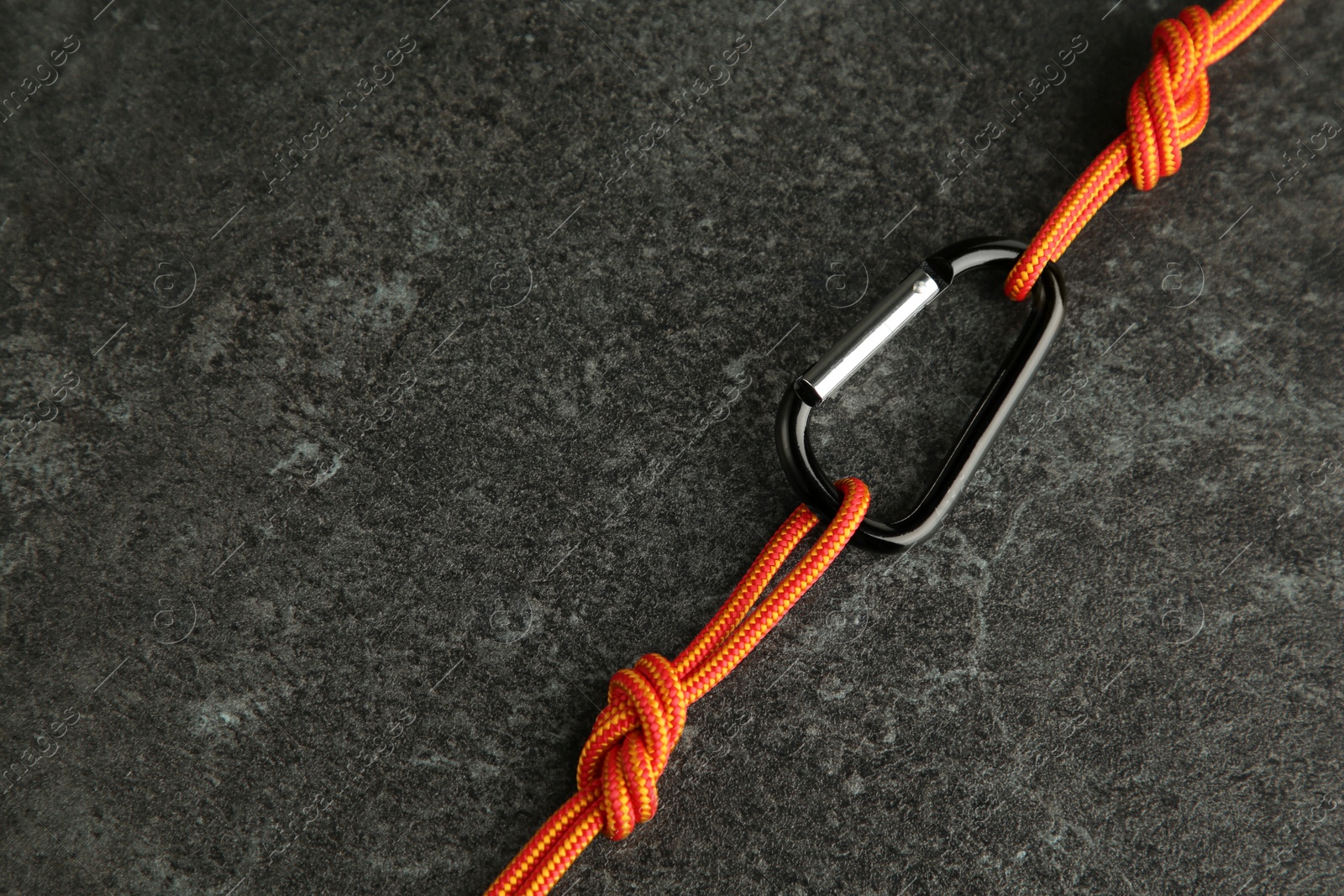 Photo of One metal carabiner with ropes on black table. Space for text