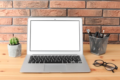 Photo of Modern laptop on table against brick wall. Mock up with space for text