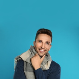 Happy young man in scarf and warm sweatshirt on blue background. Winter season